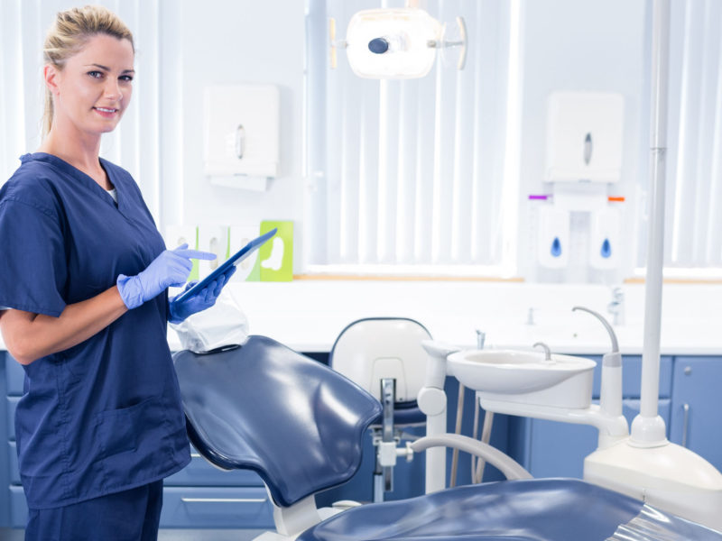 36418655 - smiling dentist working on tablet pc and looking at camera at the dental clinic